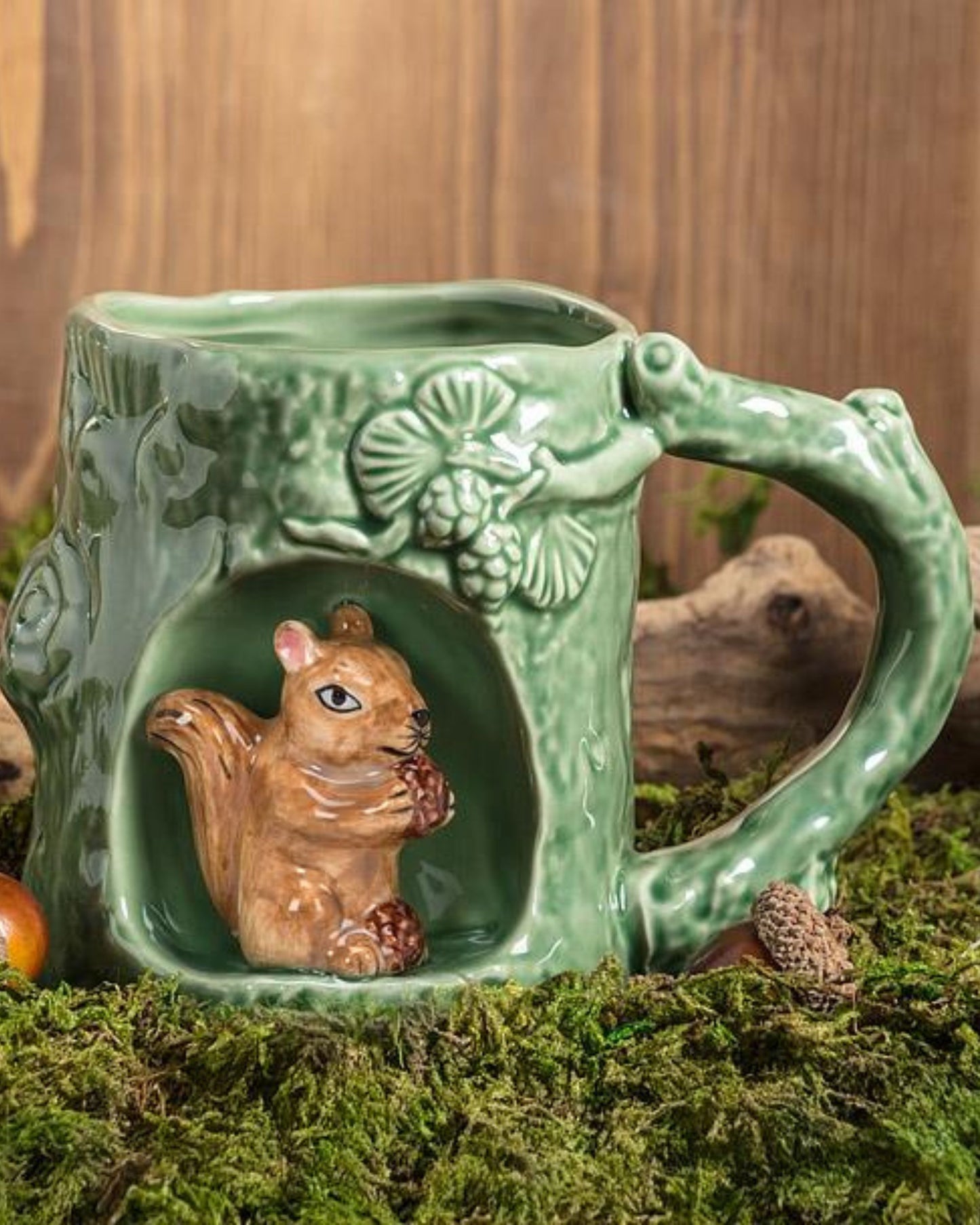 Green squirrel mug displayed on moss in a woodland-themed setting, with the squirrel figure visible in the front alcove.