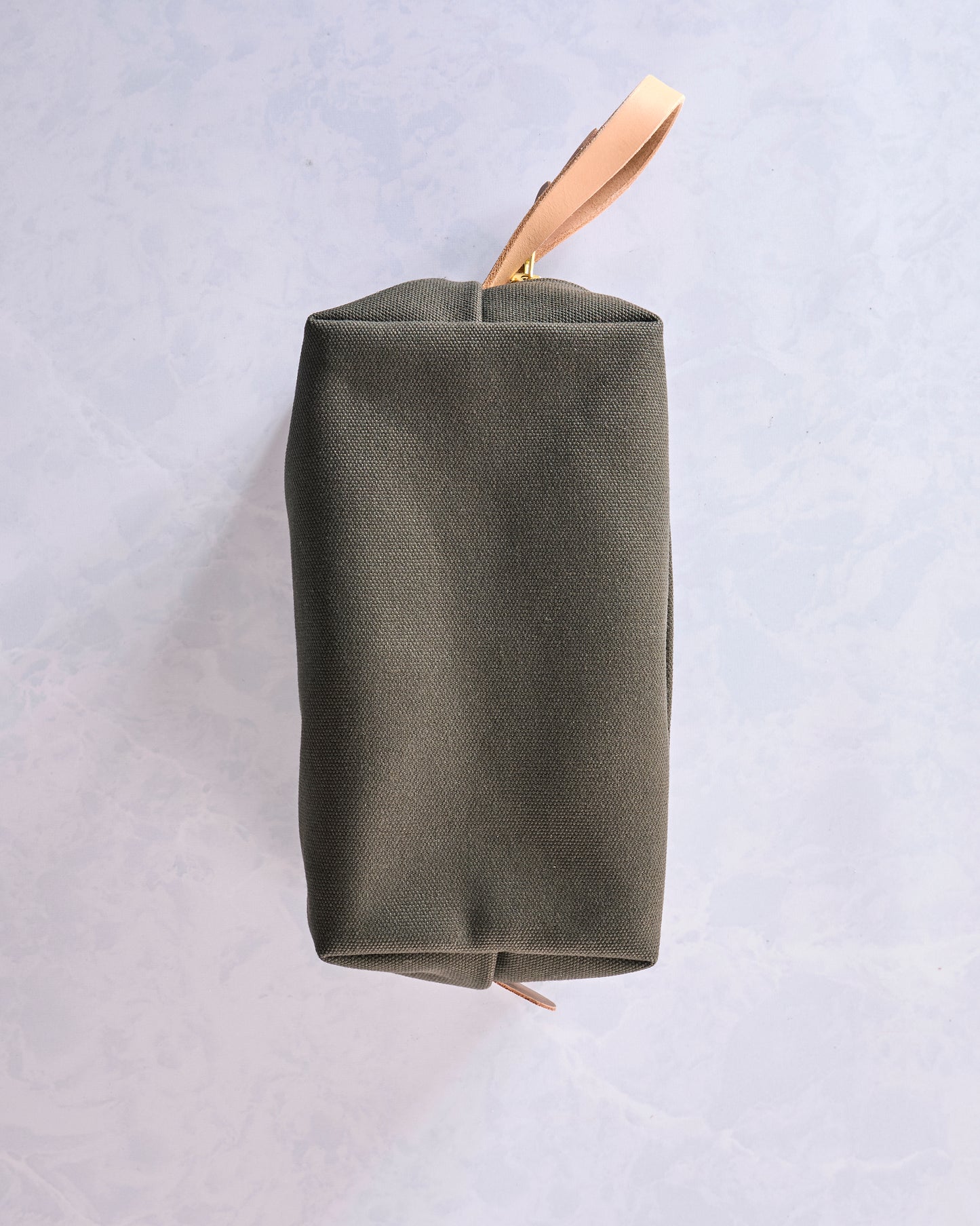 Side view of the olive canvas travel kit showing its rectangular profile and leather wrist strap.