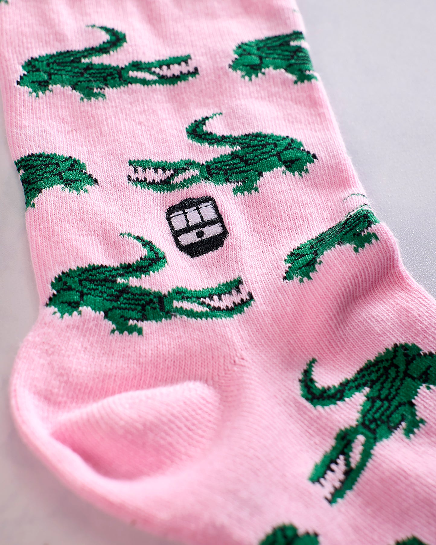 Close-up of pink socks with repeating green alligator designs and a black Bonfolk logo.
