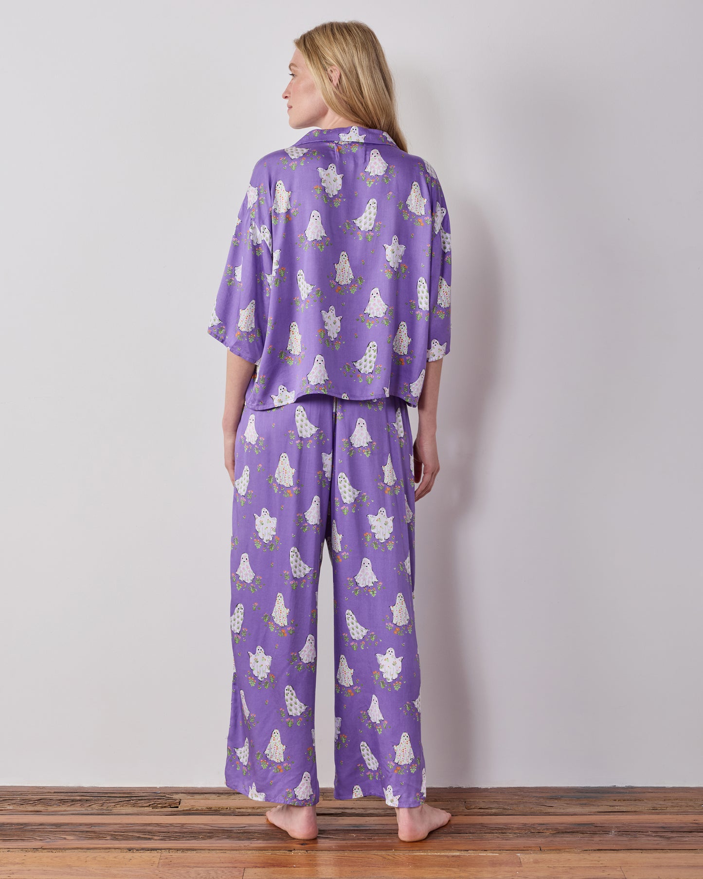 Back view of the purple Gardening Ghosts pajama set showing the collared top and wide-leg pants with a white ghost-and-floral print.
