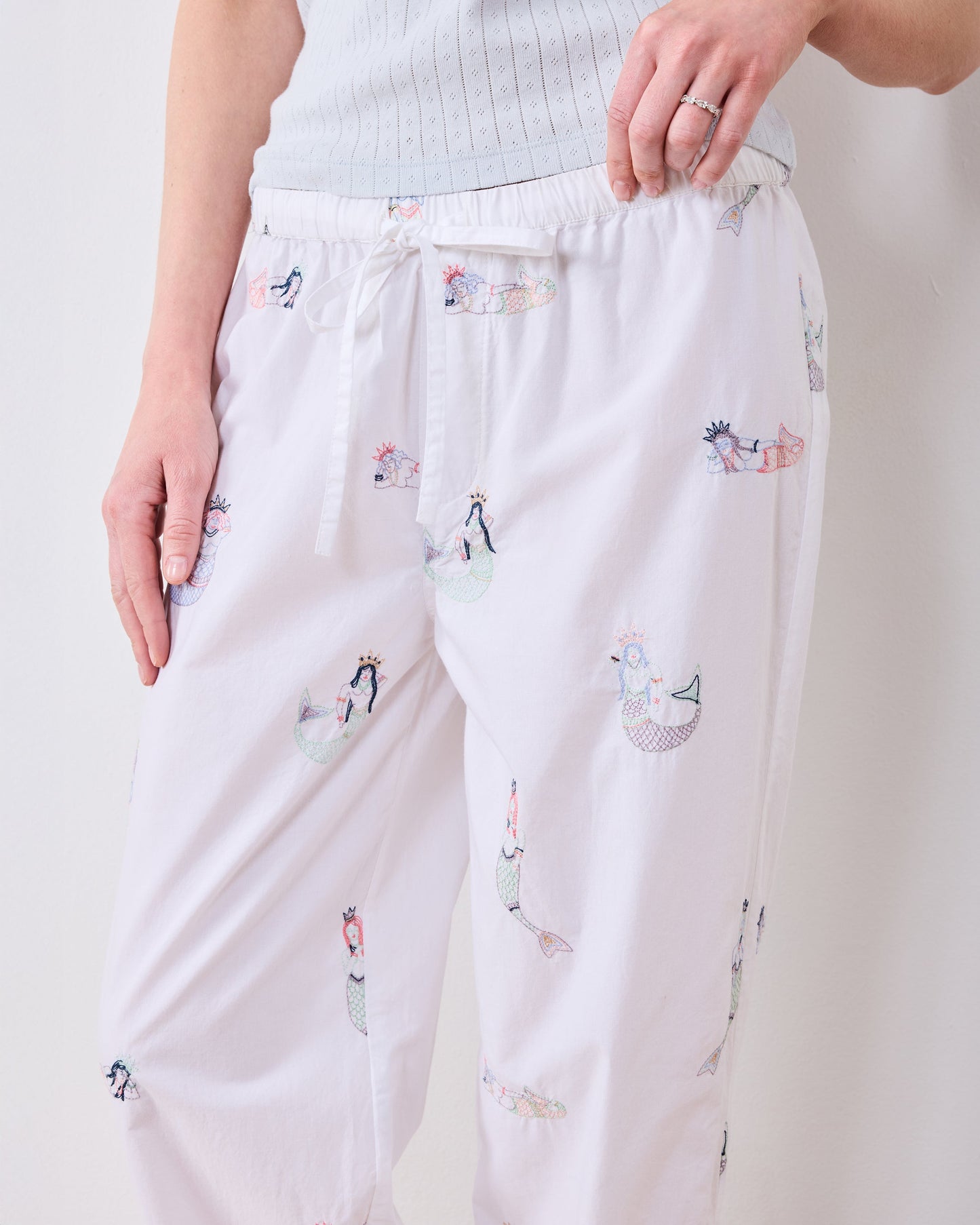 Front close-up of white mermaid pajama pants showing the elastic drawstring waist and embroidered figures