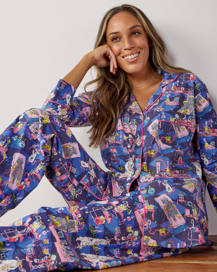 Seated model wearing the Checkered Sapphire It's Alive long pajama set, featuring a dark blue laboratory scene with mice and pink piping.