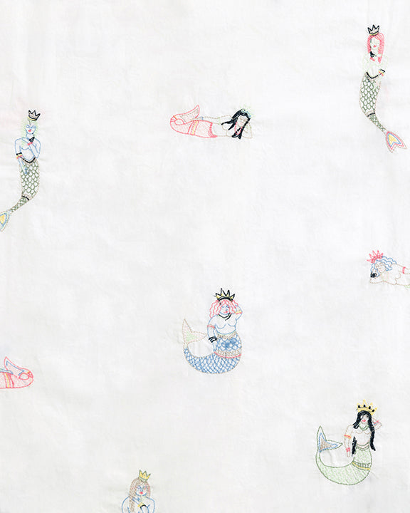 White fabric swatch with scattered multicolored mermaid motifs.