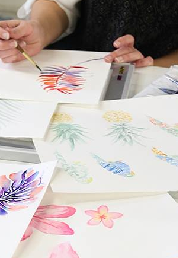 Person painting colorful floral designs on paper beside additional floral artwork
