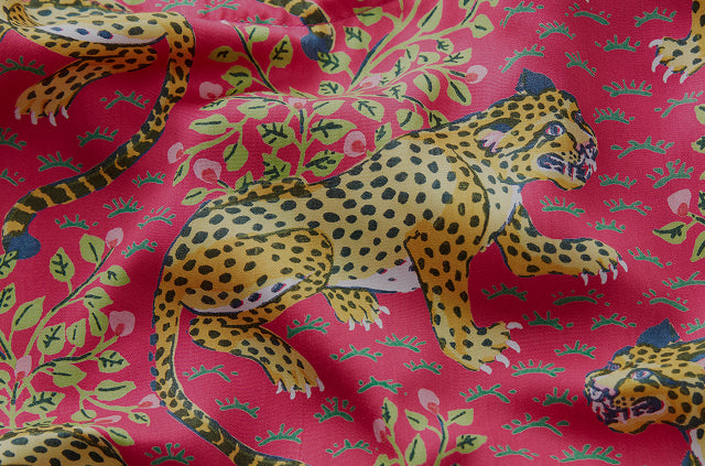 Close-up of pink textile printed with spotted leopard illustrations and leafy floral motifs.