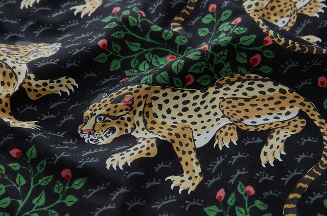 Close-up of a dark textile pattern featuring spotted leopards, green foliage, and small red flowers.