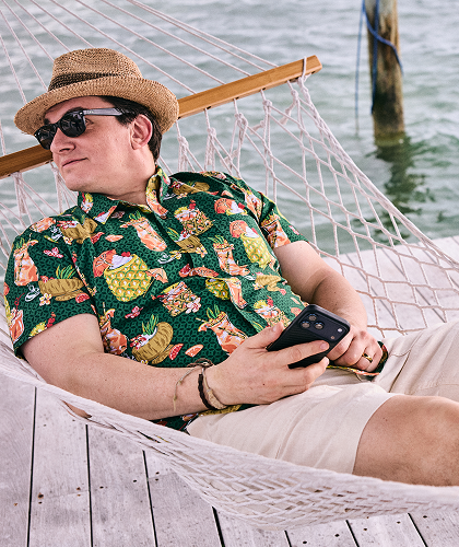 Person reclining in a hammock on a dock beside the water, holding a smartphone