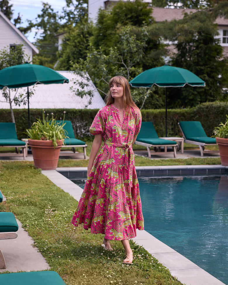 Full-length view of the hot pink Bagheera To and From Dress with leopard print, puff sleeves, tied waist belt, and full tiered skirt beside a swimming pool.