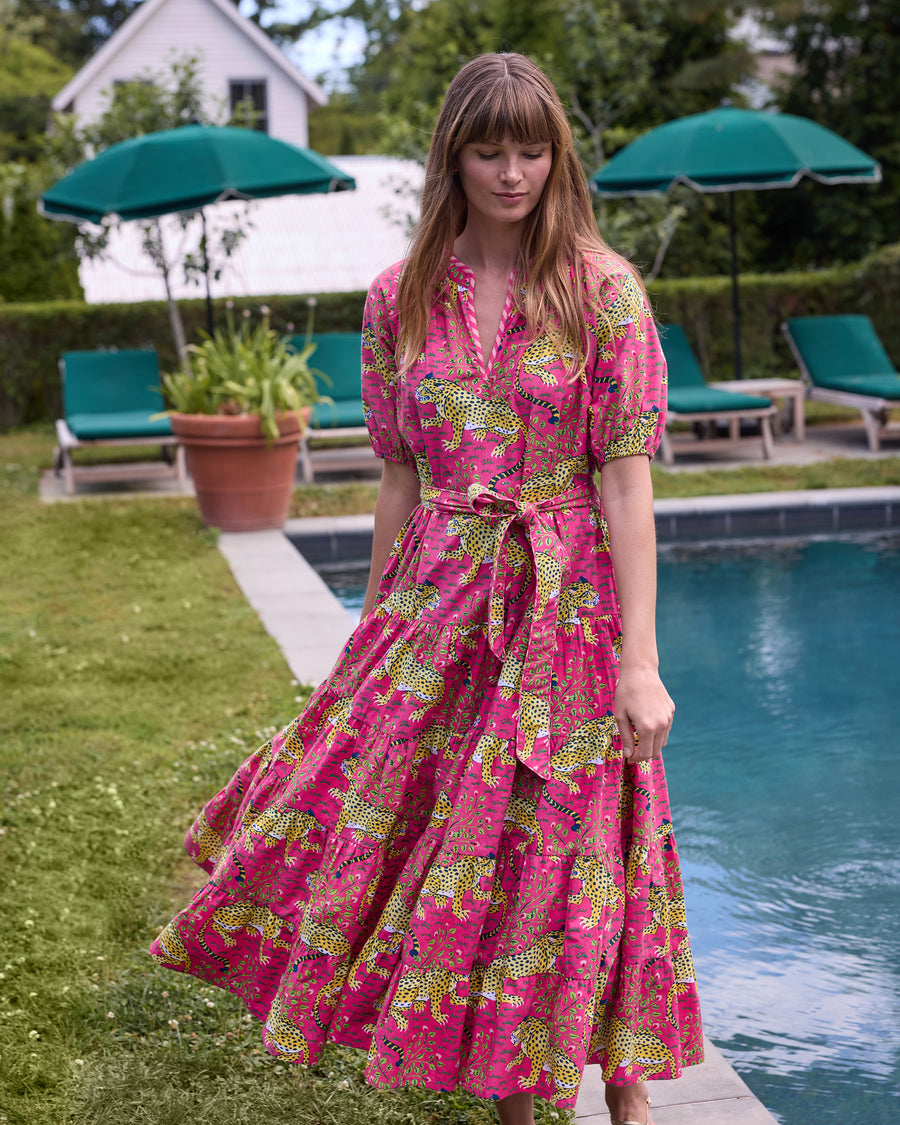 Model wearing the hot pink Bagheera To and From Dress with leopard print, puff sleeves, tied waist belt, and flowing tiered skirt beside a swimming pool.