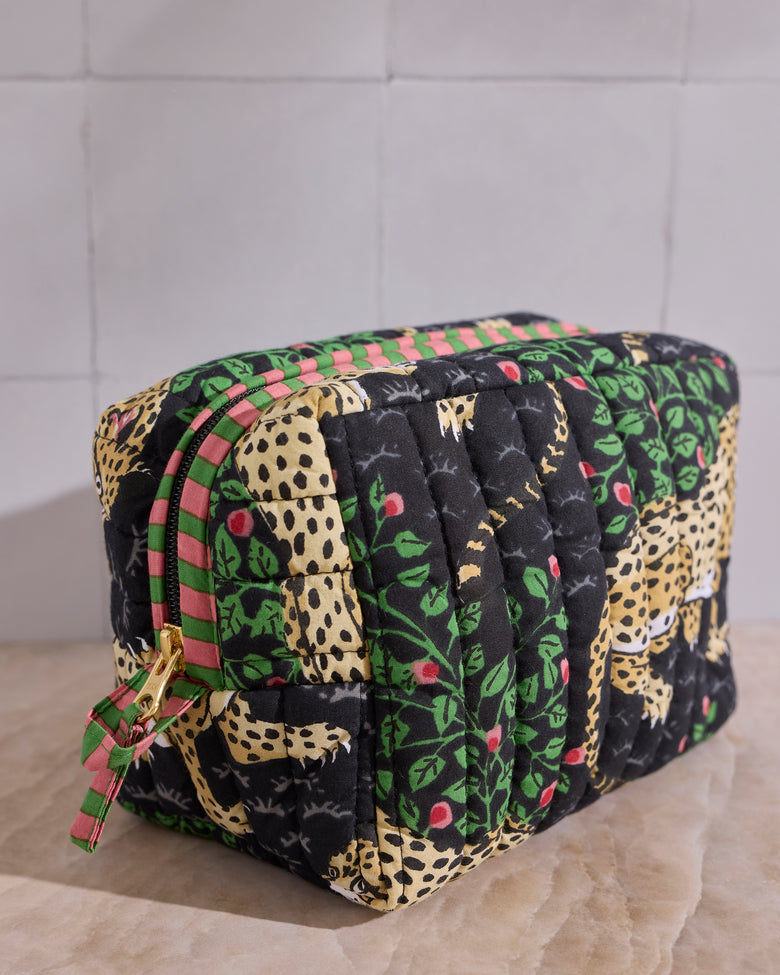 Angled view of the Ink Bagheera quilted pouch, showing its padded vertical quilting, leopard-and-leaf print, zipper, and wristlet tab.