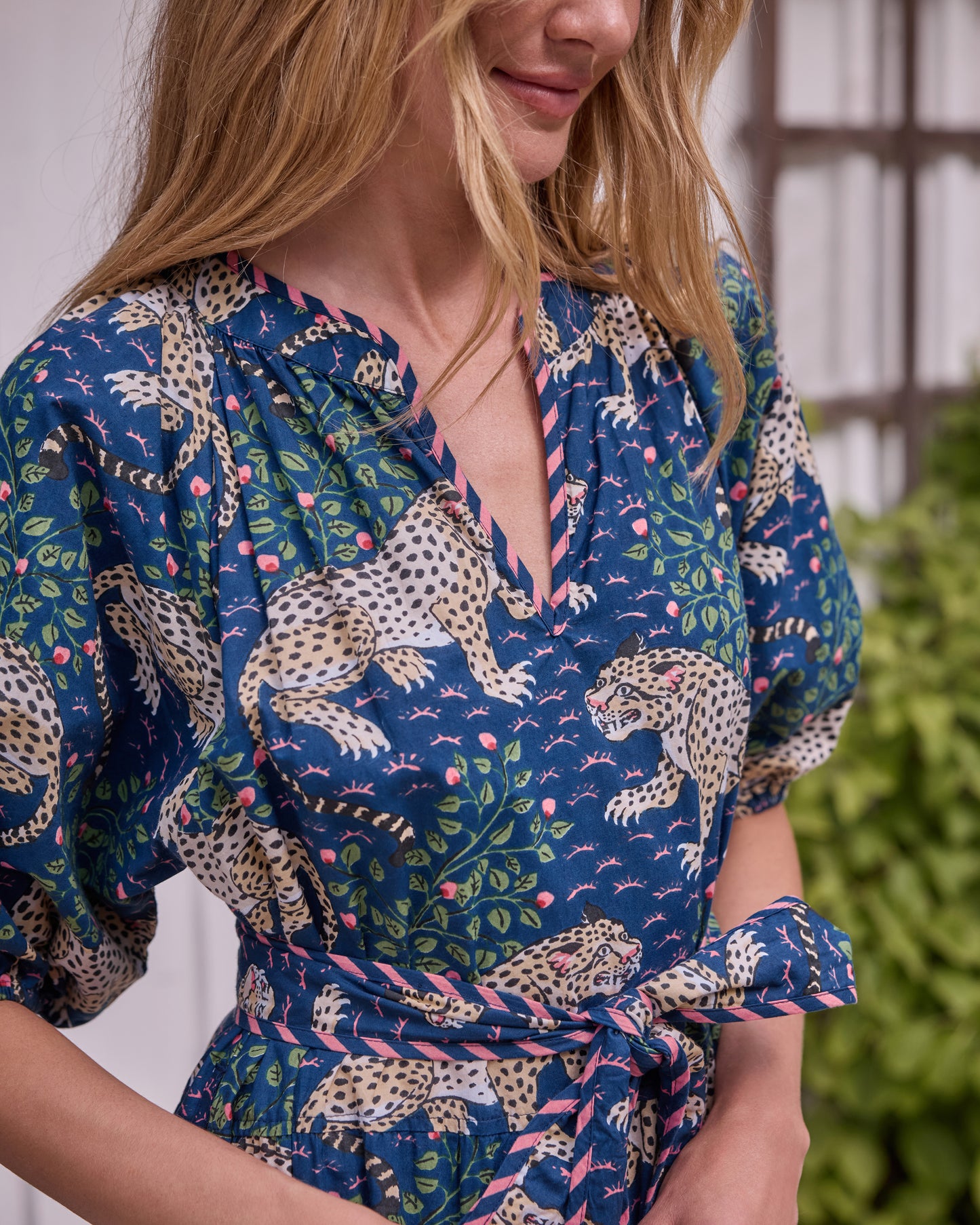 Close view of the Bagheera dress showing its V-neckline, leopard-and-floral print, puff sleeve, and tied waist belt.
