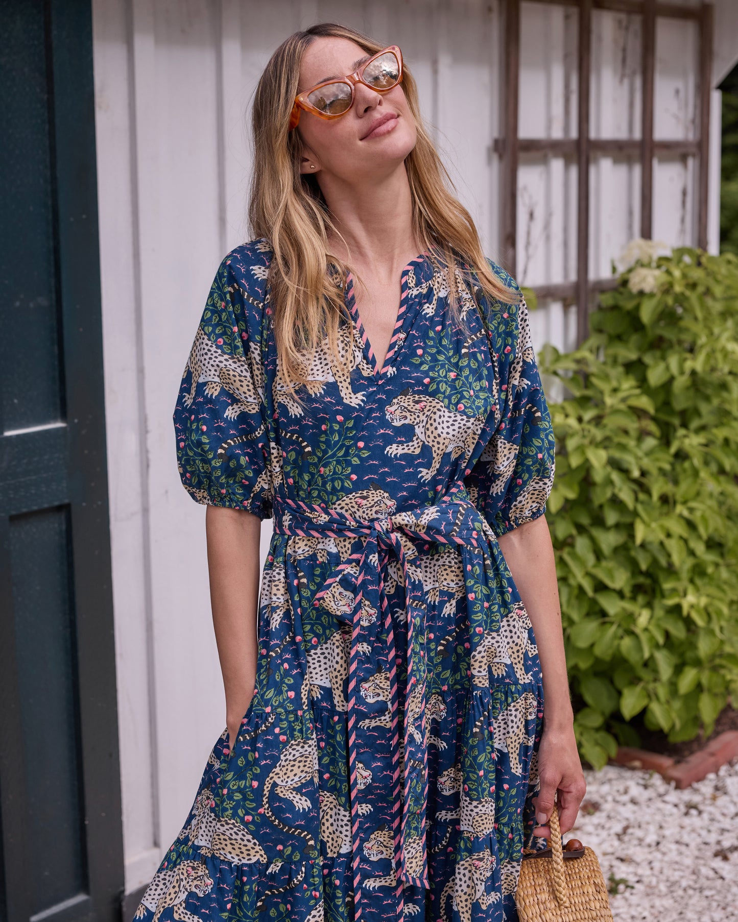 Front view of the navy Bagheera dress with leopard-and-floral print, tied belt, puff sleeves, and a woven handbag.
