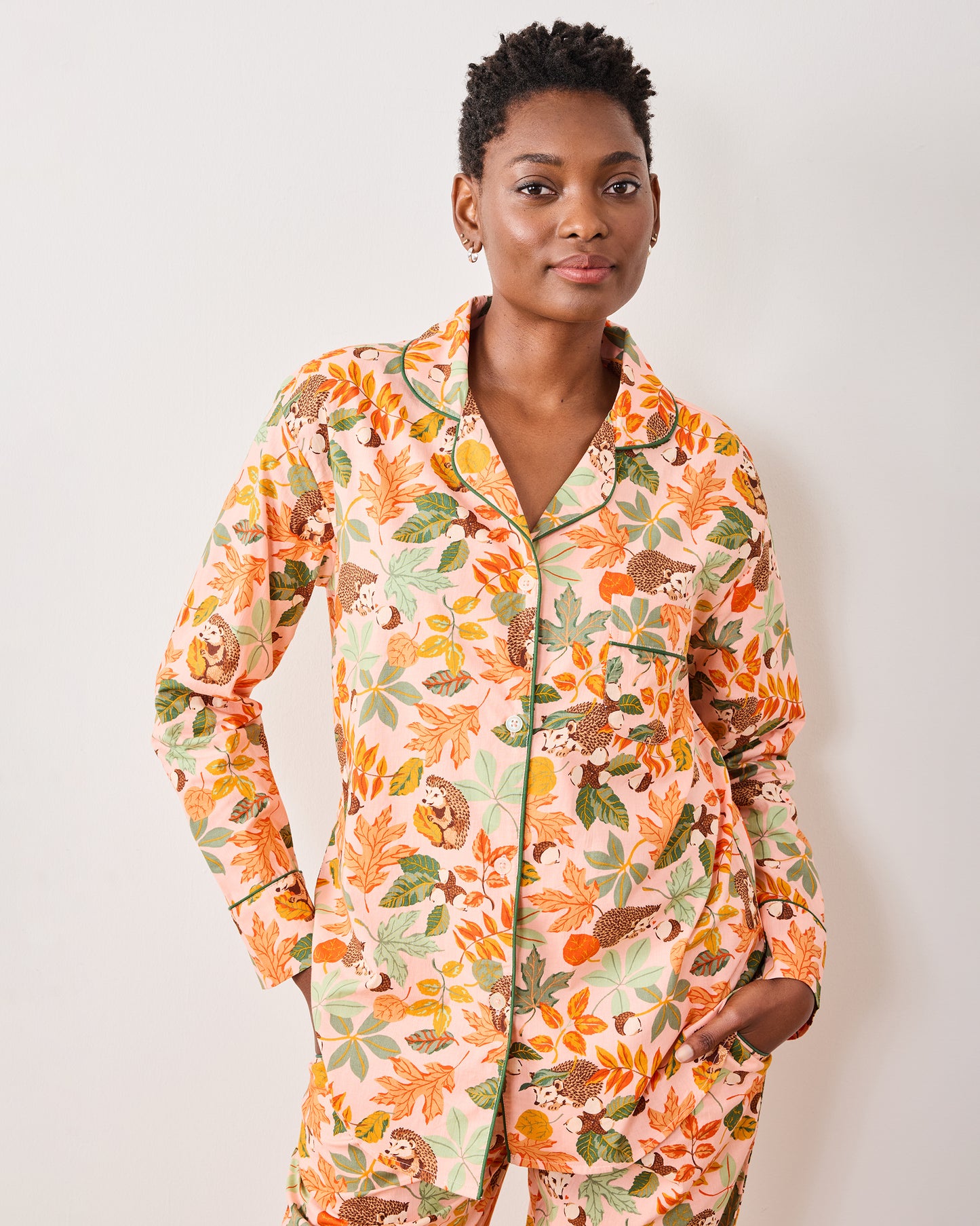 Front view of a model wearing the peach button-down pajama set with hedgehogs and autumn foliage.