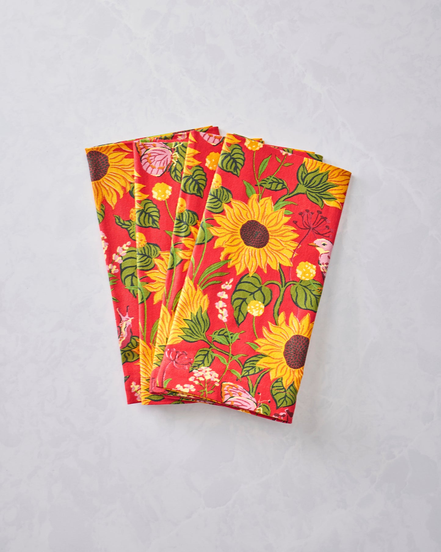 Folded orange napkins with a sunflower, leaf, and bird print.