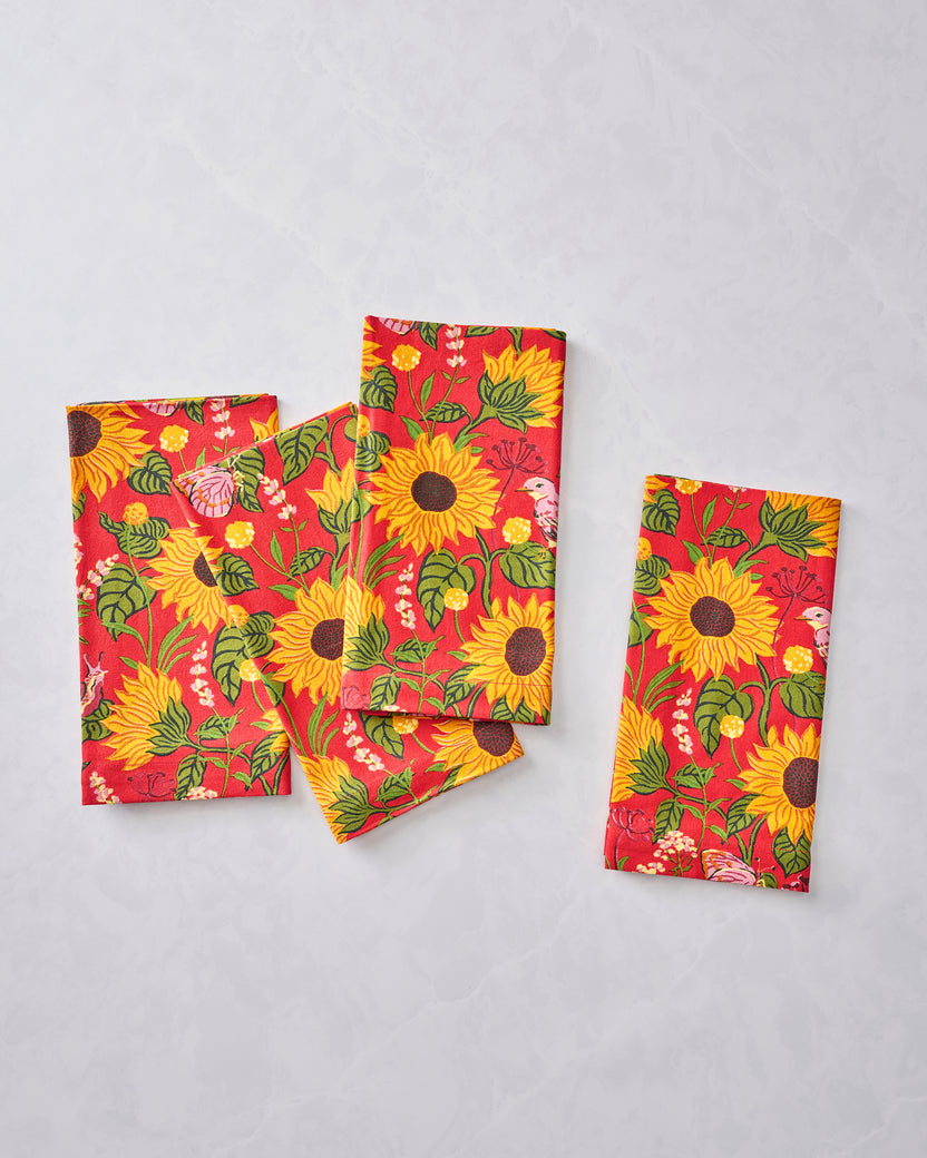 Four orange napkins arranged separately to show their sunflower, leaf, and bird print.