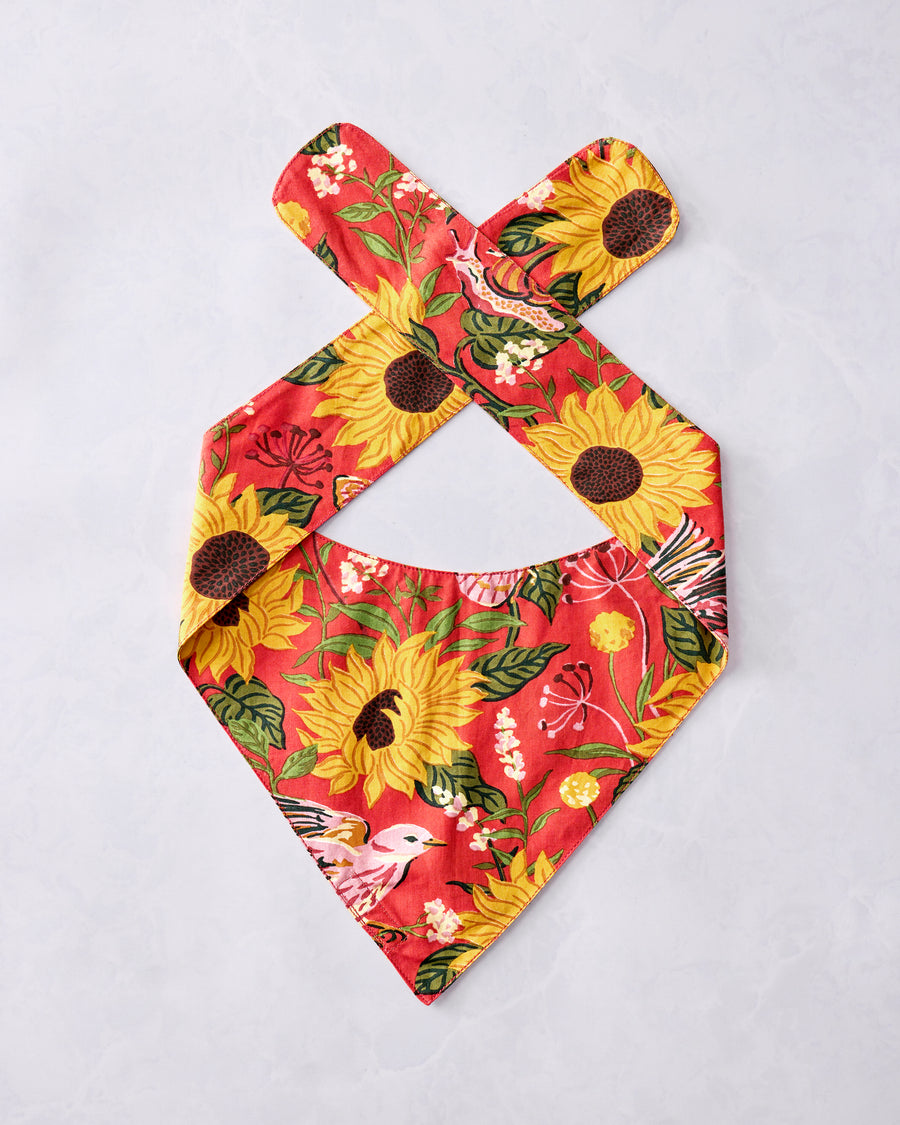 Orange pet bandana with a sunflower, bird, leafy floral, and butterfly print, laid flat with crossed neck straps.