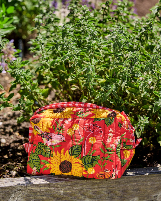 Orange quilted pouch with a sunflower, bird, leaf, and snail print, photographed outdoors on a wooden surface.
