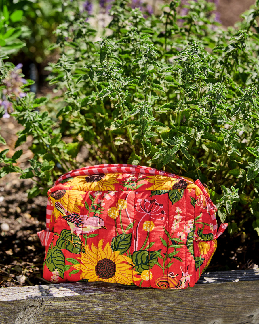 Orange quilted pouch with a sunflower, bird, leaf, and snail print, photographed outdoors on a wooden surface.