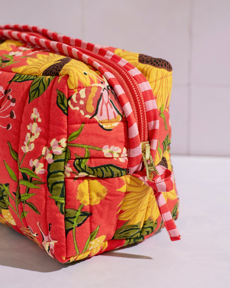 Close-up of the quilted pouch showing its orange floral print, pink-and-white striped trim, zipper, and gold-tone pull.