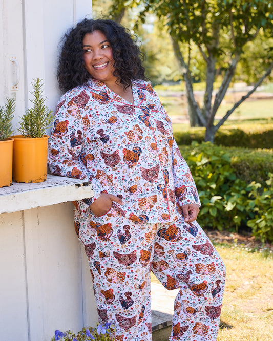 Lifestyle view of the Must Love Chickens pajama set, showing a long-sleeved button-front top and pants with a chicken-and-floral print.