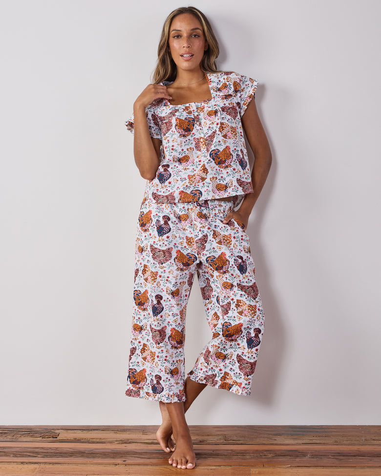 Model standing and wearing a cropped pajama top with flutter sleeves and matching wide-leg pants in a chicken-and-floral print.