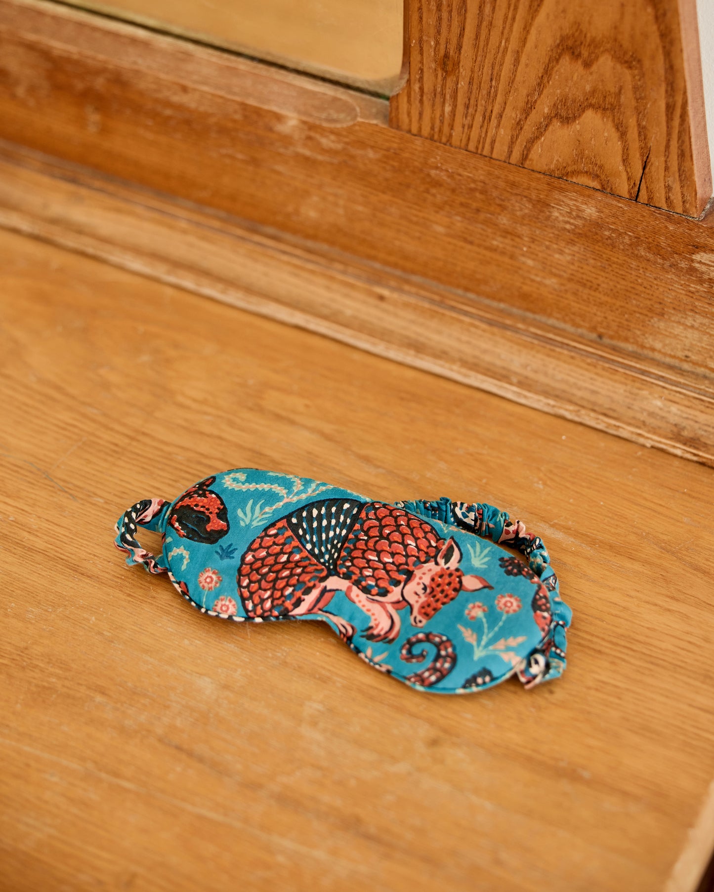 Teal Southwestern Critters eyemask displayed on a wooden floor, showing its printed front and elastic strap.