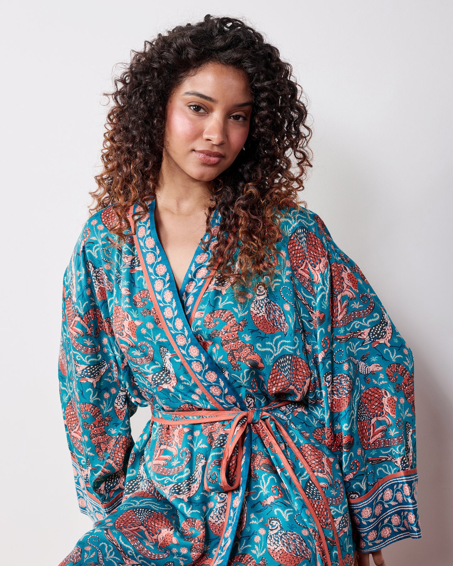 Front view of a person wearing the teal Southwestern Critters satin robe with long sleeves, a wrap front, and waist belt.