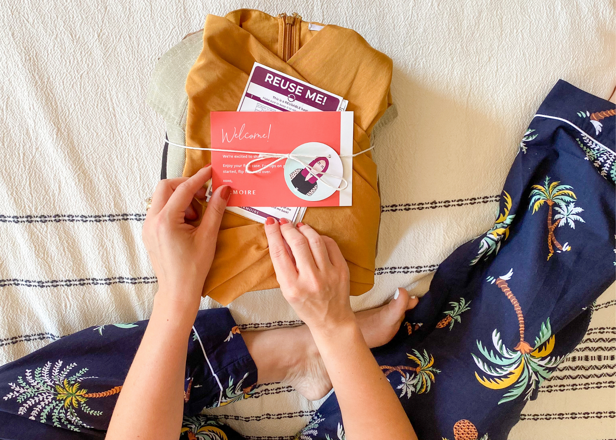 Person holding a welcome card over folded clothing and a package labeled “REUSE ME!”