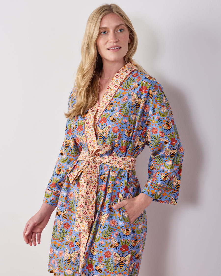 Person wearing the Delphinium Blue Bee Tapestry robe, showing its floral and bee print, shawl collar, matching belt, and pockets.