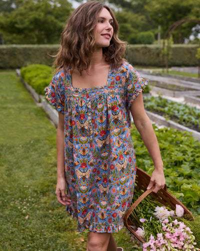 Three-quarter view of the Delphinium Blue Bee Tapestry pintuck nightgown, showing its button-front neckline, short sleeves, ruffled hem, and floral bee print.