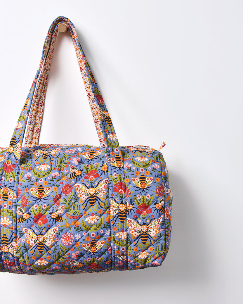 Close-up of the blue Bee Tapestry quilted duffle bag, showing its bee-and-floral print, handles, and top zipper.