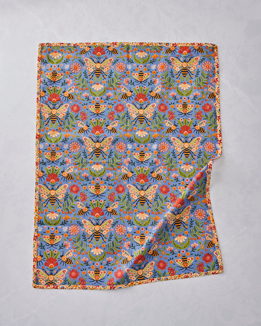 Bee Tapestry tea towel shown flat with a repeating blue floral-and-bee pattern and a narrow cream patterned border.