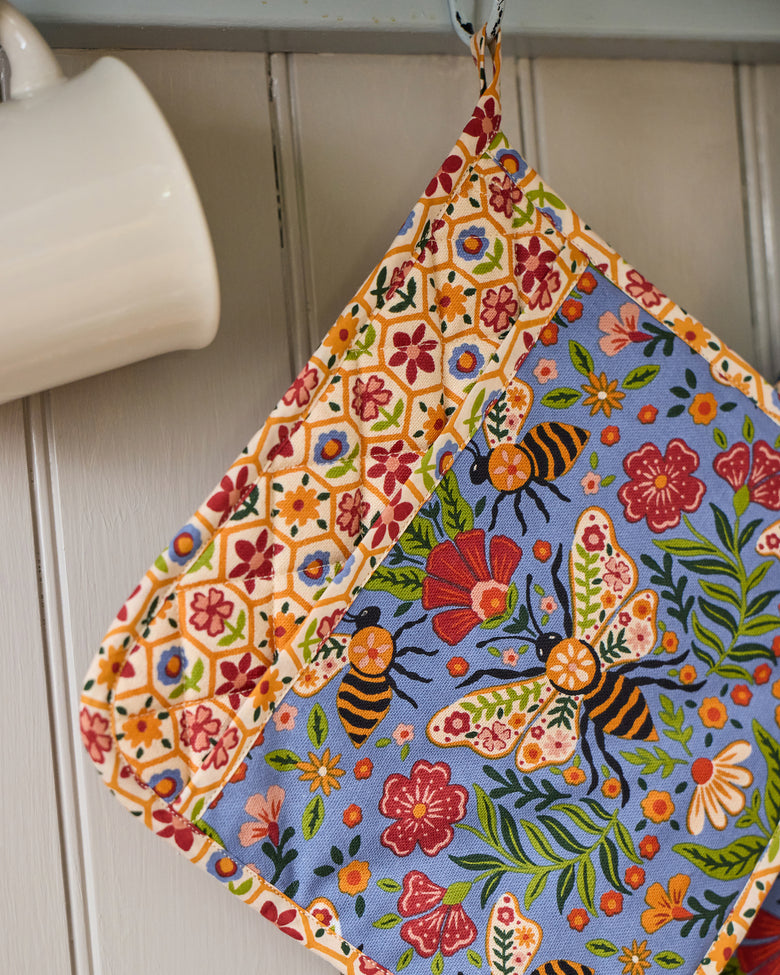 Bee Tapestry pot holder hanging from a hook, with a blue floral-and-bee center and cream floral-patterned border.