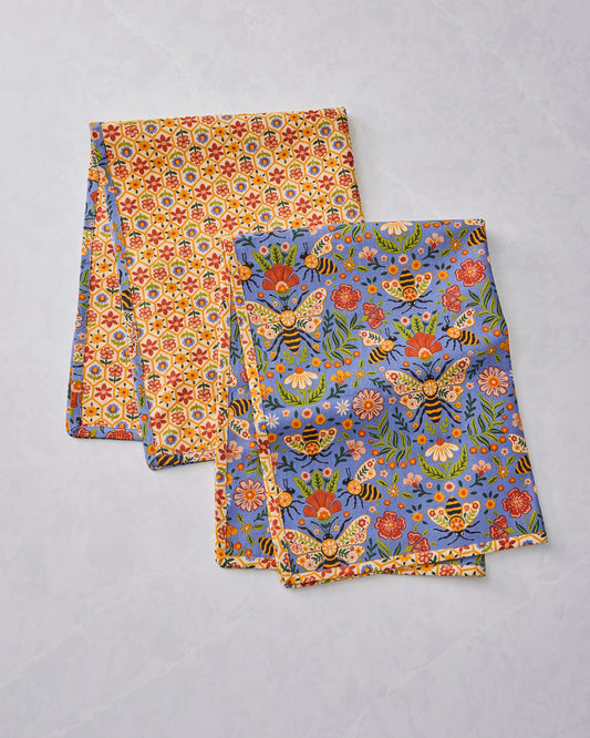 Two Bee Tapestry tea towels displayed overlapping, with one floral-patterned towel and one blue towel covered in bees and flowers.