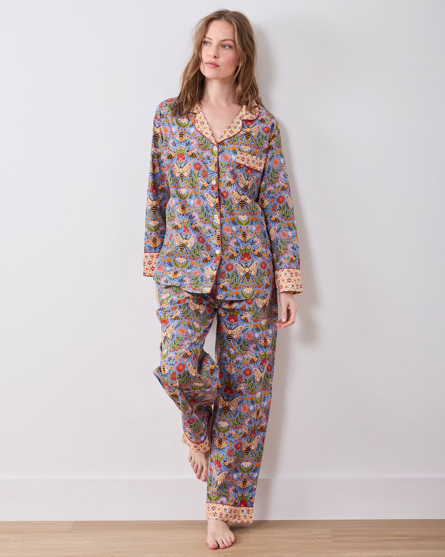 Full-length front view of a long-sleeve button-front pajama top and matching pants with a blue bee-and-floral print and contrasting collar, cuffs, and pant hems.