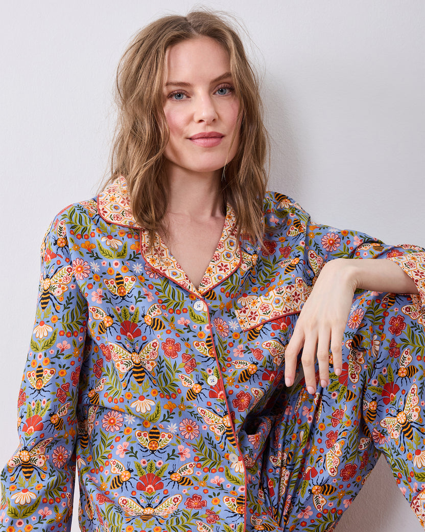 Seated front view of the Bee Tapestry Delphinium Blue petite long pajama set, showing the printed button-down top and matching pants.