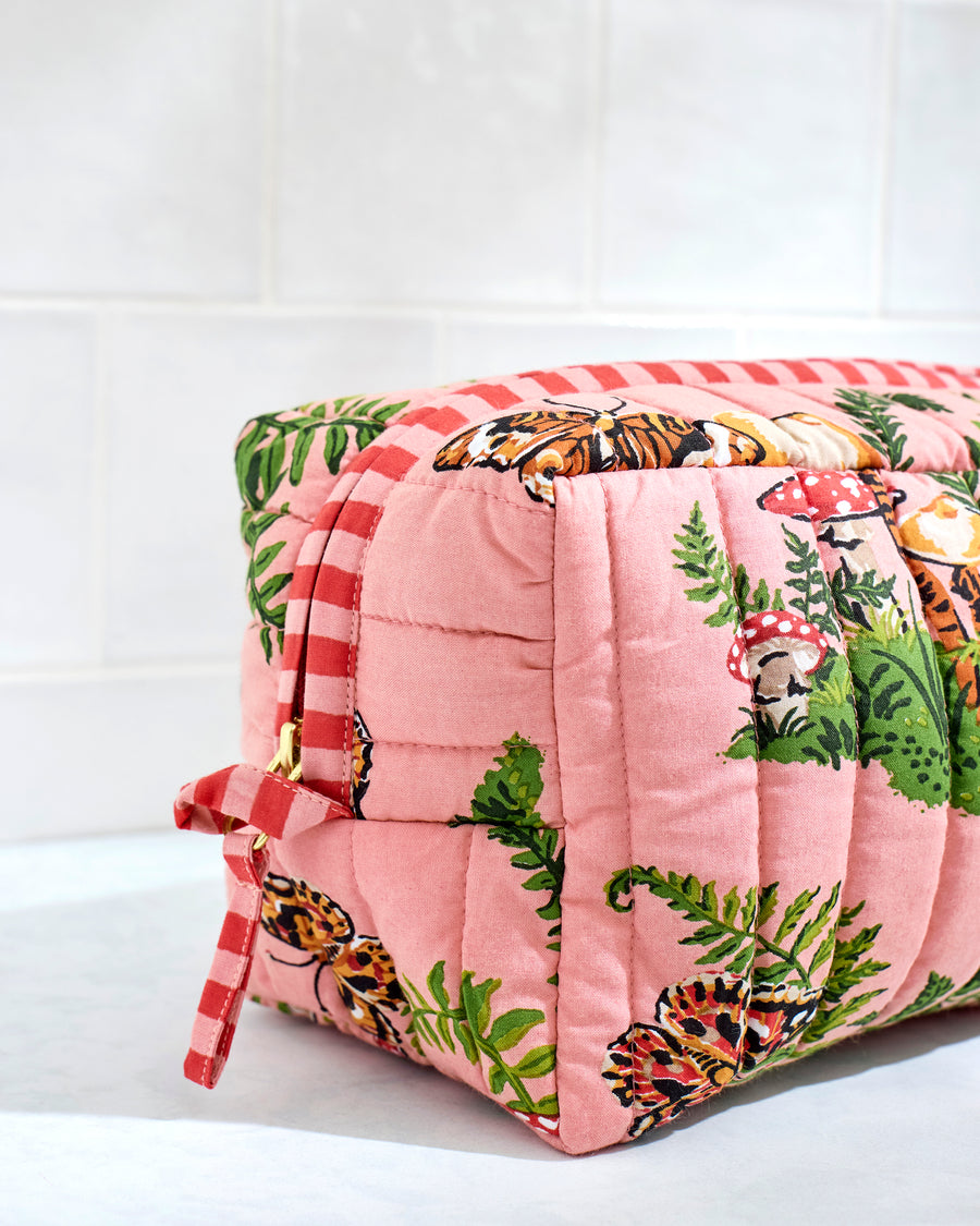 Angled side view of a quilted butterfly-print pouch showing its striped trim, side tie, and printed mushrooms and ferns.