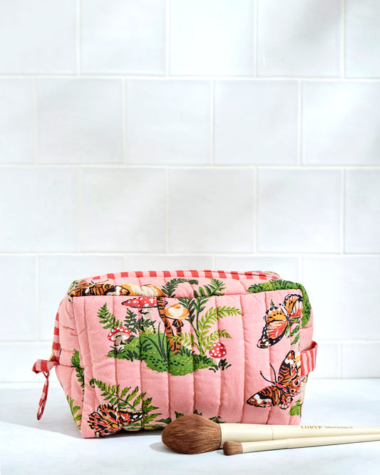 Front view of a quilted butterfly-print pouch with mushrooms and ferns, shown beside makeup brushes.