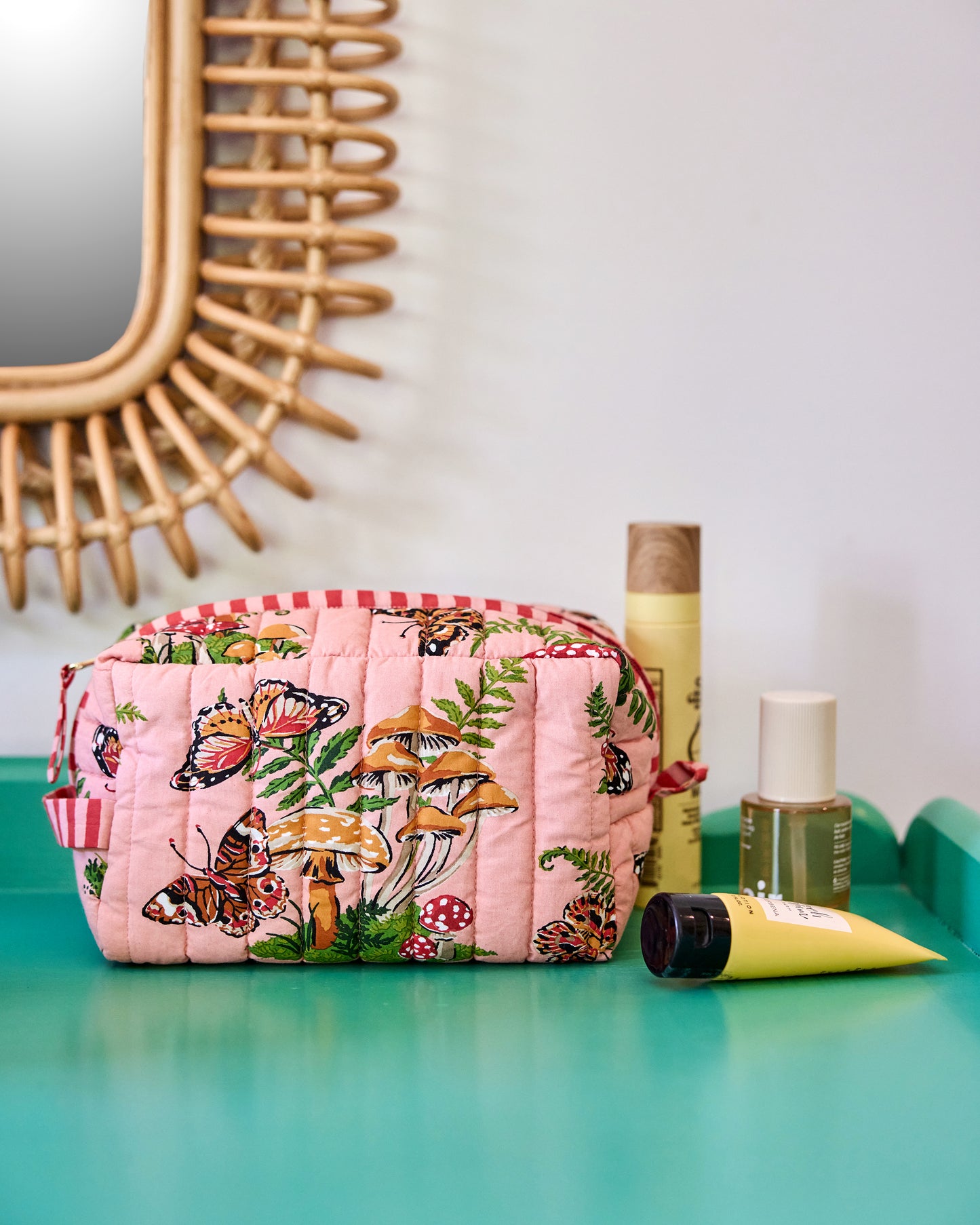Quilted butterfly-print pouch displayed beside cosmetic containers on a turquoise surface.