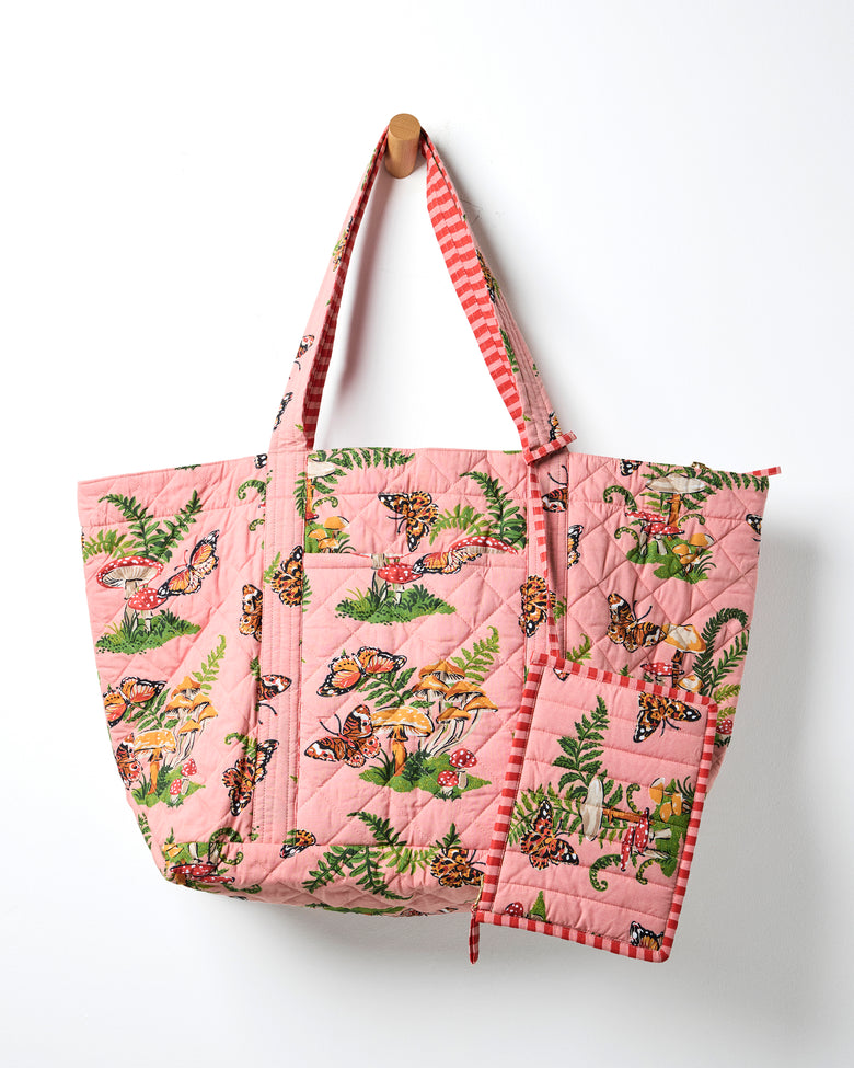 Rosewood quilted weekend bag with matching pouch, featuring butterflies, mushrooms, and ferns; the bag hangs from a wall peg.