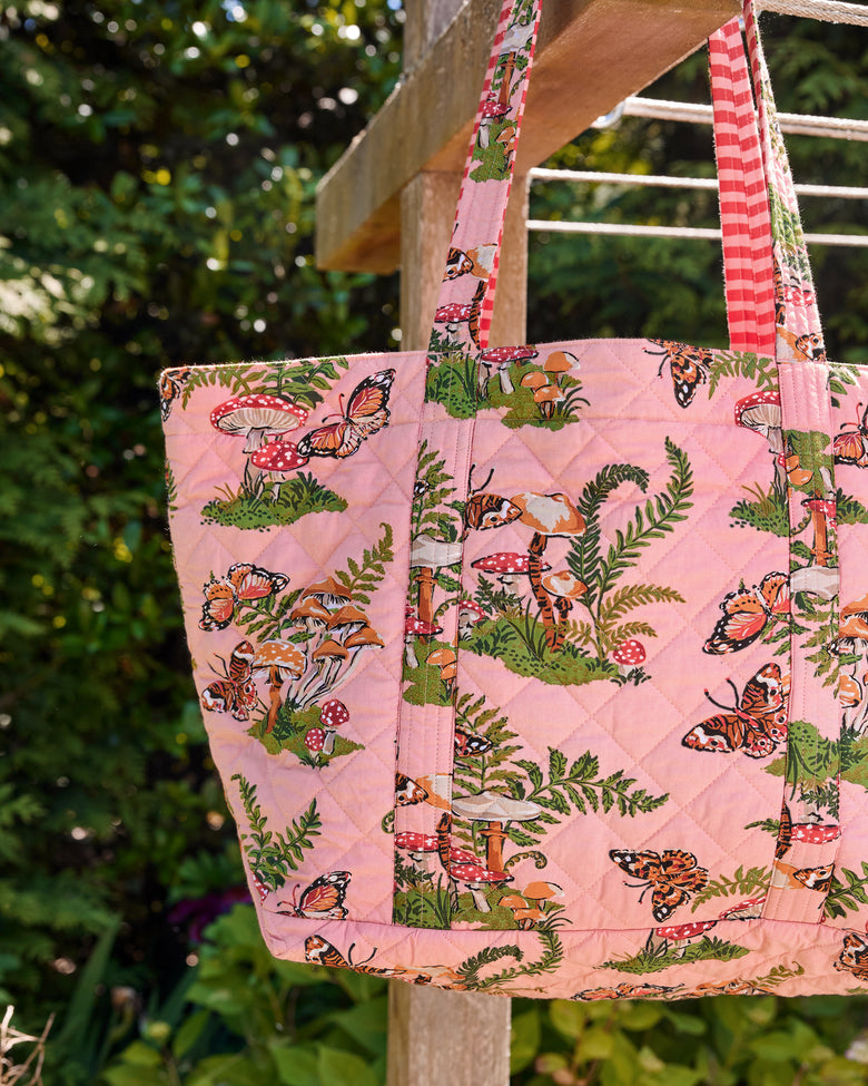 Close-up of the rosewood quilted weekend bag showing its butterfly, mushroom, and fern print, straps, and attached pouch.
