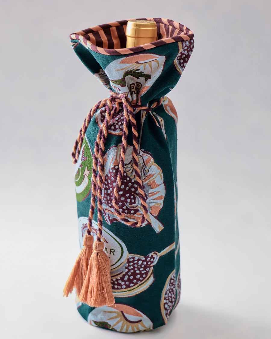 Champagne & Caviar wine bag standing upright with a bottle inside, showing its patterned exterior, gathered top, braided tie, and peach tassels.