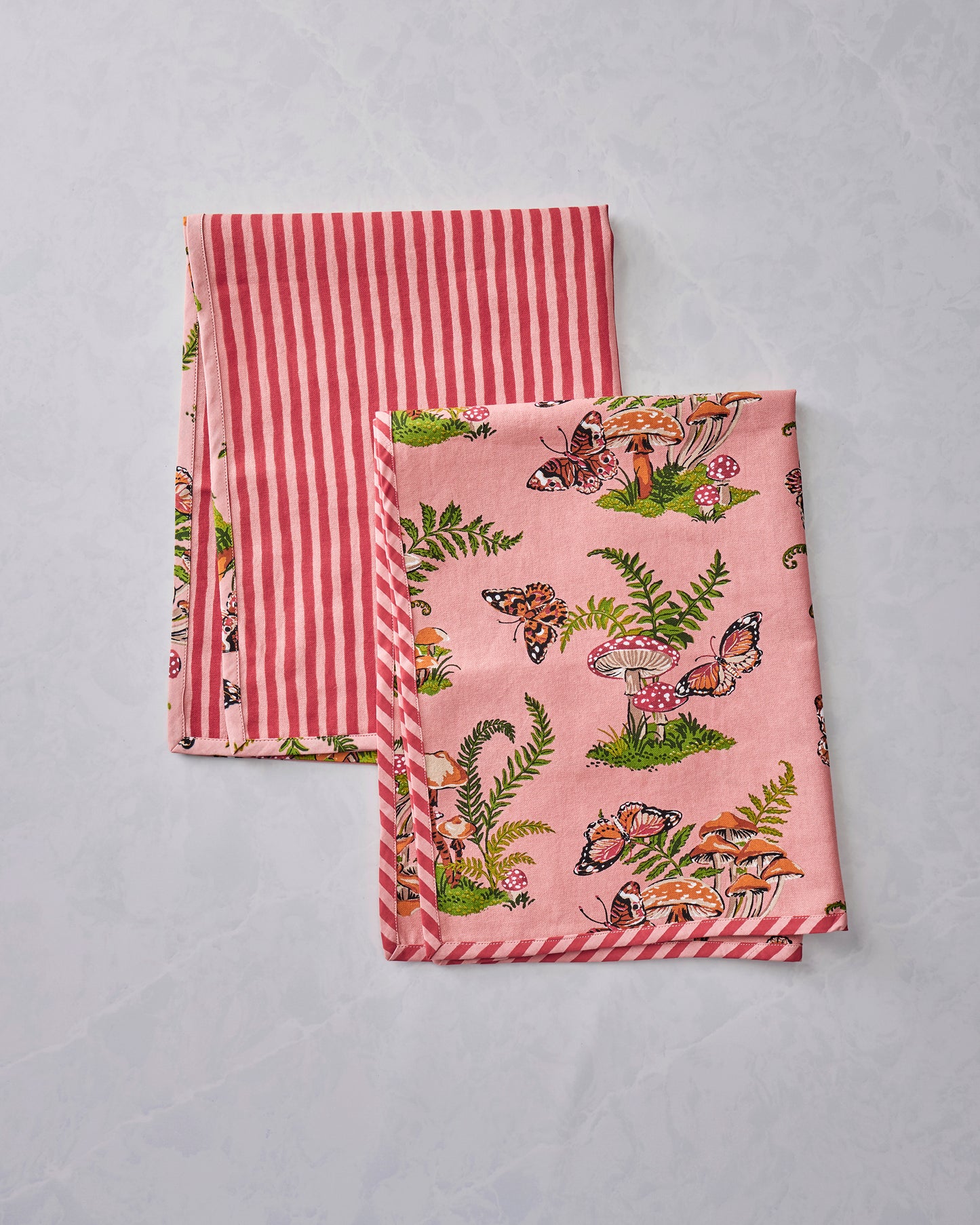 Two Butterfly Forager tea towels folded together, showing the pink butterfly, mushroom, and fern print with red-and-white striped borders.