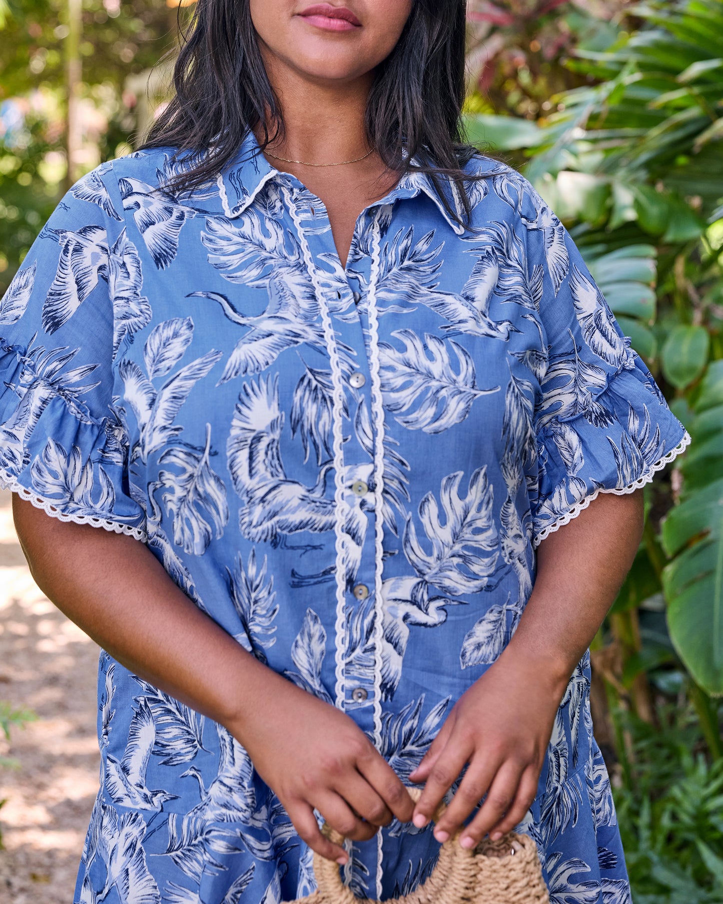 Close front detail of the blue Estelle Dress showing the heron print, buttons, scalloped trim, and ruffled sleeves