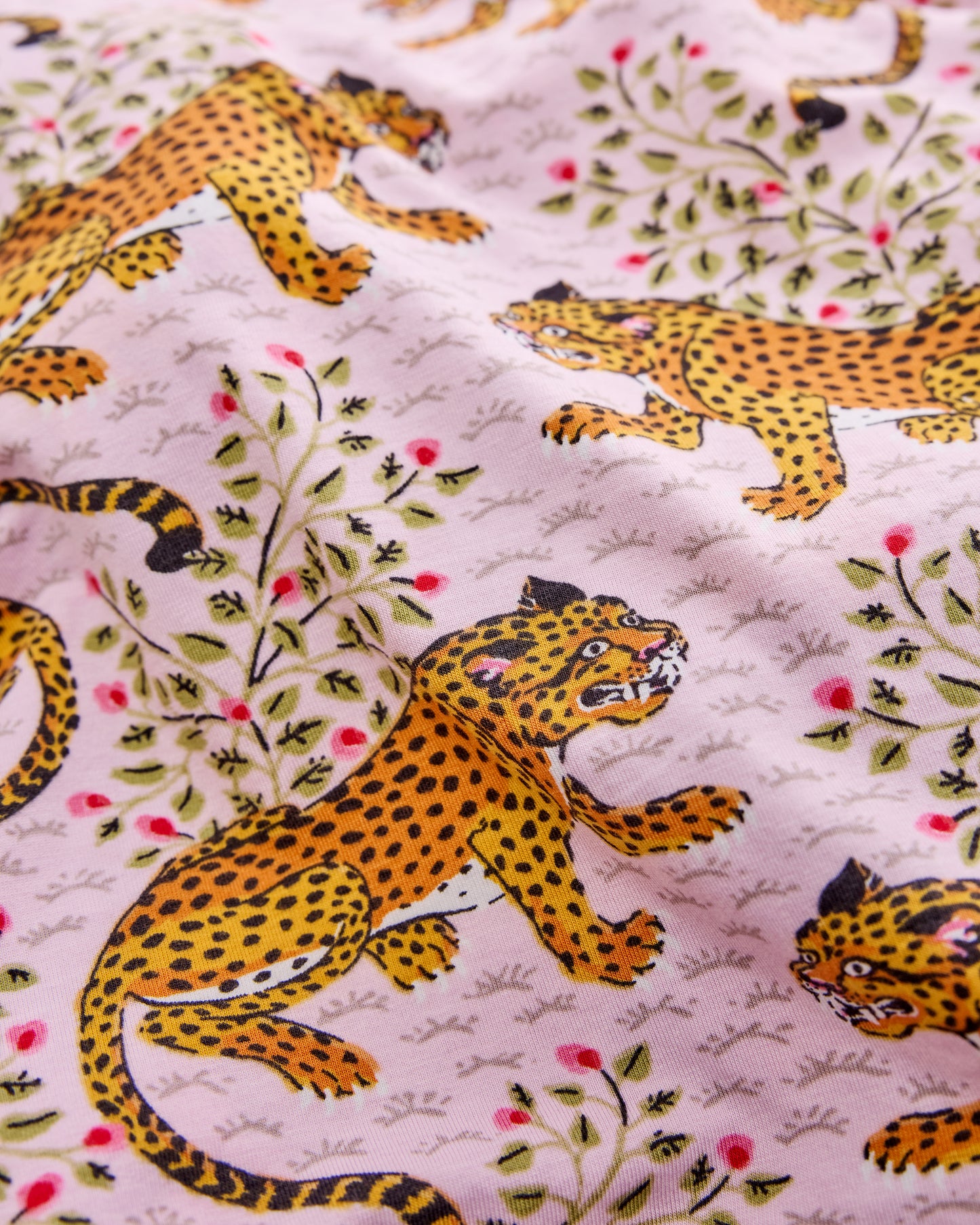 Close-up of the Bagheera leopard print on blush fabric, showing spotted leopards, leafy branches, and small red floral accents.