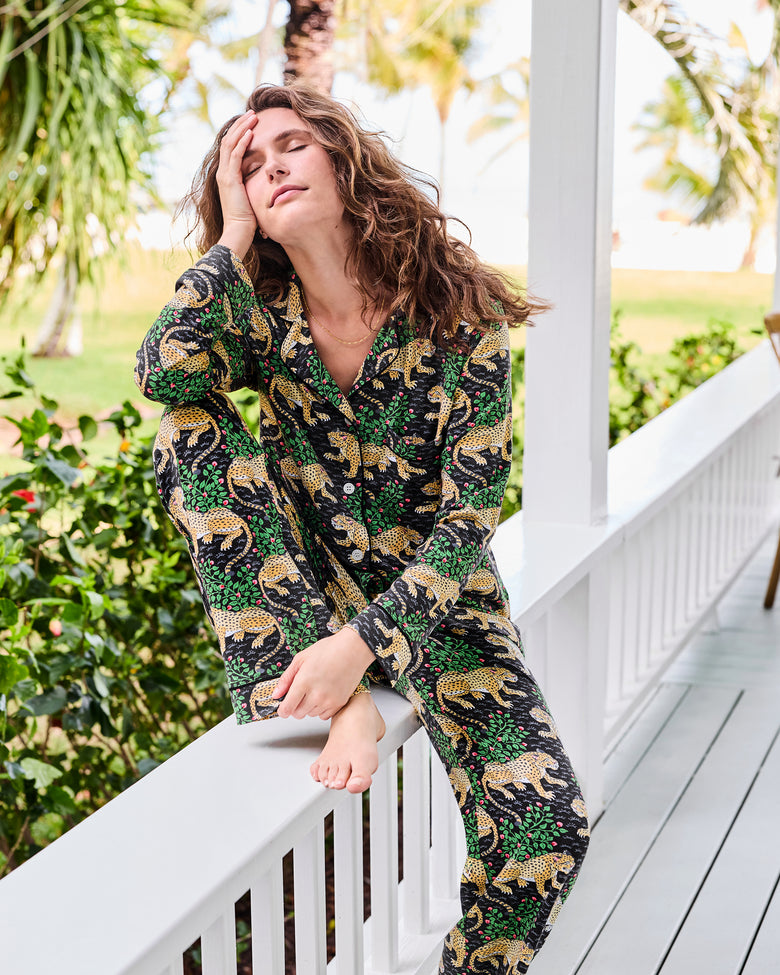 Person sitting on a porch railing wearing a black long-sleeve leopard-and-floral print pajama set.
