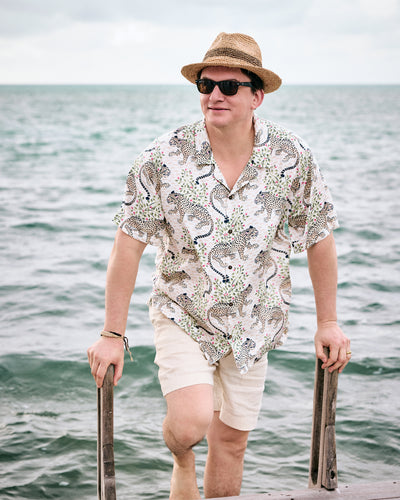 Front view of the Wedding Cake camp shirt with a leopard and foliage print, worn by the water