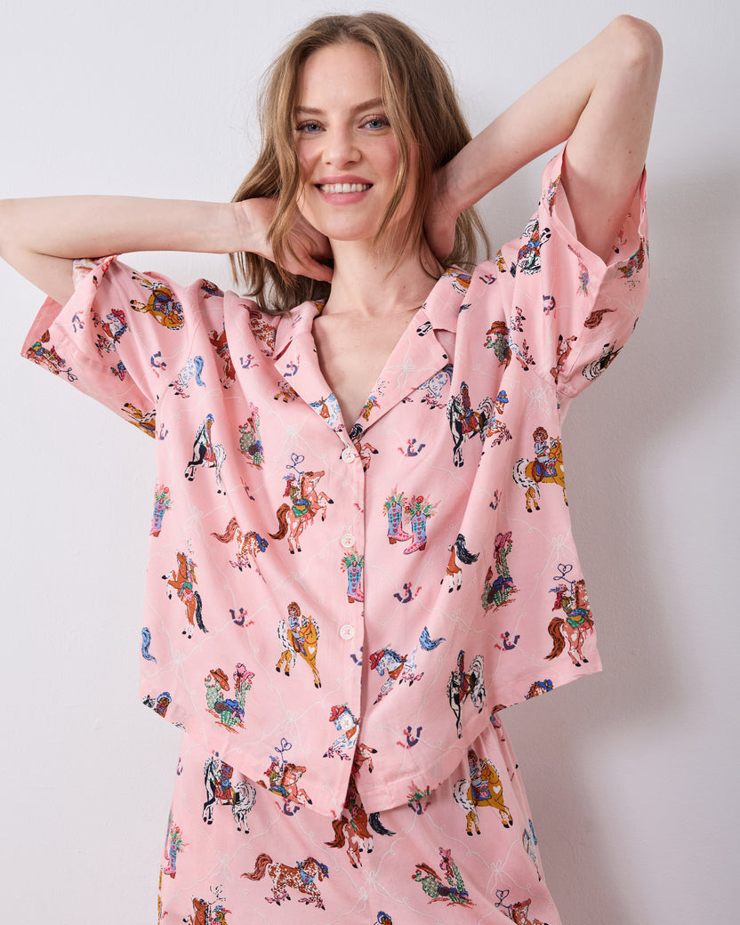 Model wearing the pink cowgirl-print petite pajama top and matching pants with her arms raised.