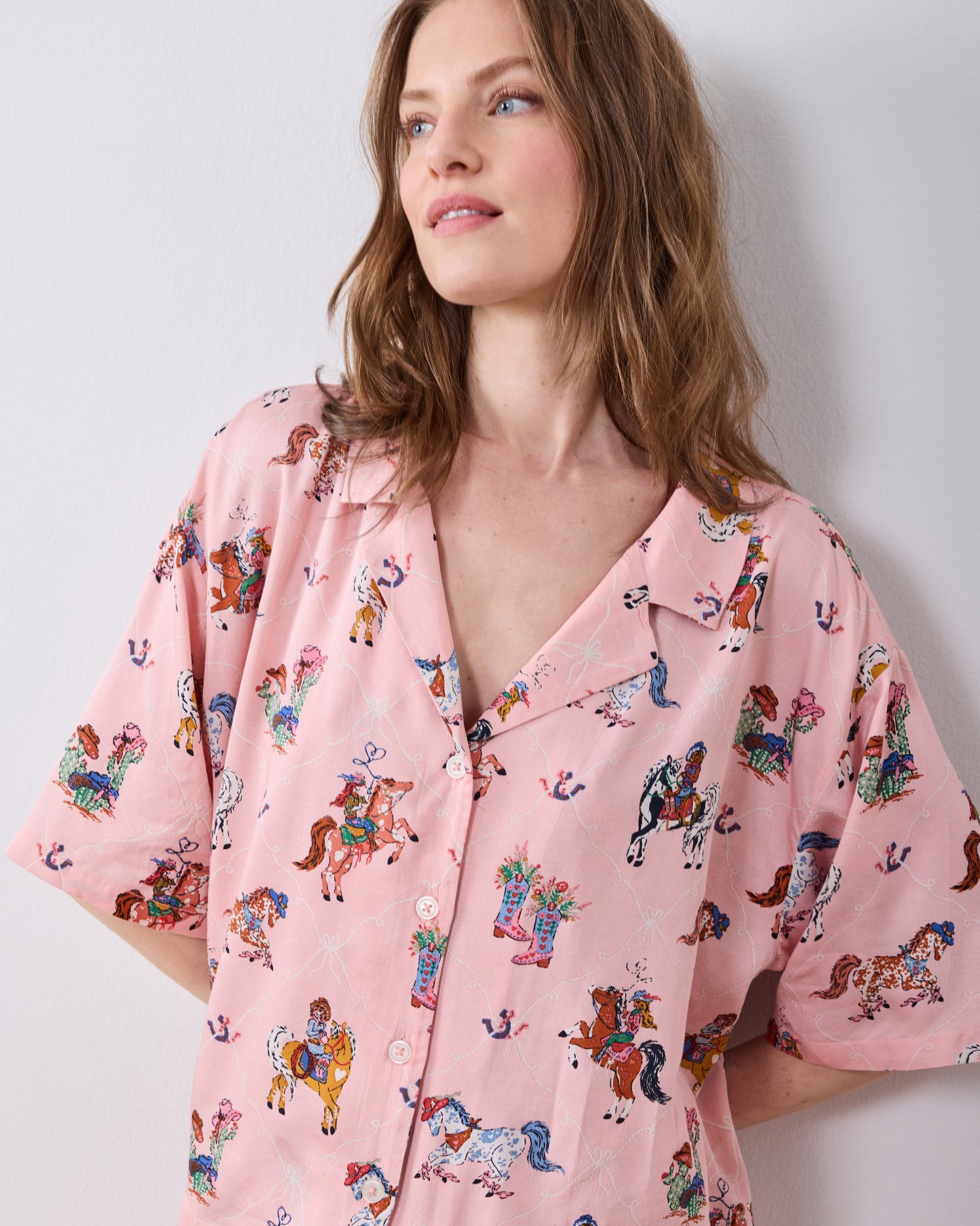 Close-up of a model wearing the pink long pajama top with a notched collar, front buttons, and horse-and-cowgirl print.