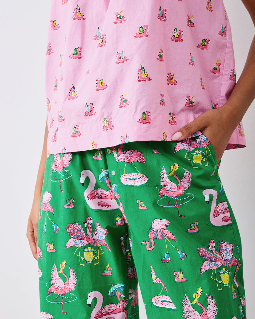 Close view of the pink cami hem and green flamingo-print cropped pants with a hand in the pocket